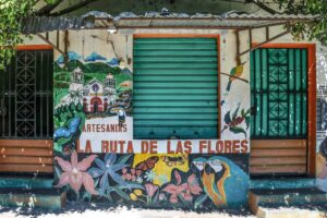 El Salvador Highlights: Five Day Tour A colorful building facade displays a mural with flowers, butterflies, birds, and the words "Artesanias La Ruta de las Flores" in Spanish.