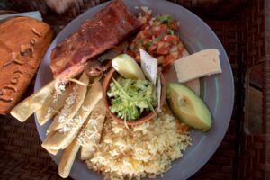San Salvador Cooking Workshop With Pupusas A plate with food items including meat, rice, cheese, avocado, tortillas with cheese, and a small bowl of green salad.
