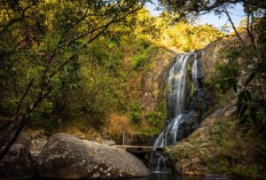 A Taste Of El Salvador (7 days) A scenic view of a waterfall cascading over rocks into a pool, surrounded by lush green trees and vegetation.