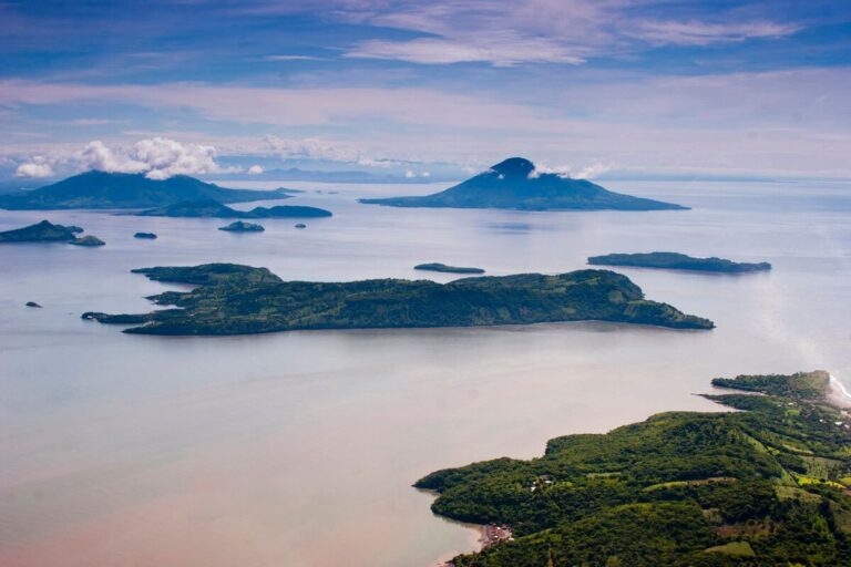 An aerial shot showcases several lush islands scattered across a vast expanse of water, under a partly cloudy sky.