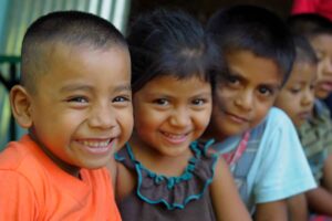 El Salvador Complete Travel (21 days) A close-up shows four smiling children of color huddled together, with the first three in focus, wearing a variety of colored clothing.