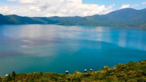 One Week In El Salvador: Option 2 A scenic view of a turquoise lake surrounded by lush green mountains under a partly cloudy sky.