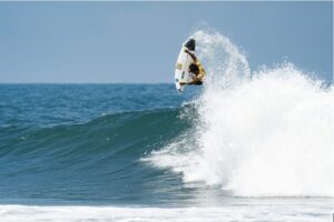 Facts About El Salvador You Probably Didn’t Know A surfer performs an aerial maneuver on a wave, spraying water into the air against a blue sky and sea background.