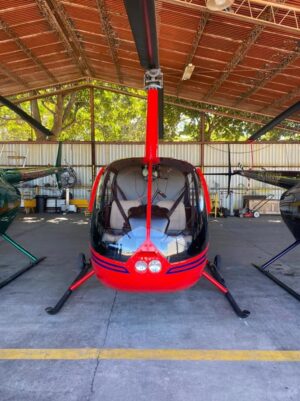 Helicopter Charter In El Salvador A red helicopter is parked in a hangar, flanked by two other helicopters, one green and one black.
